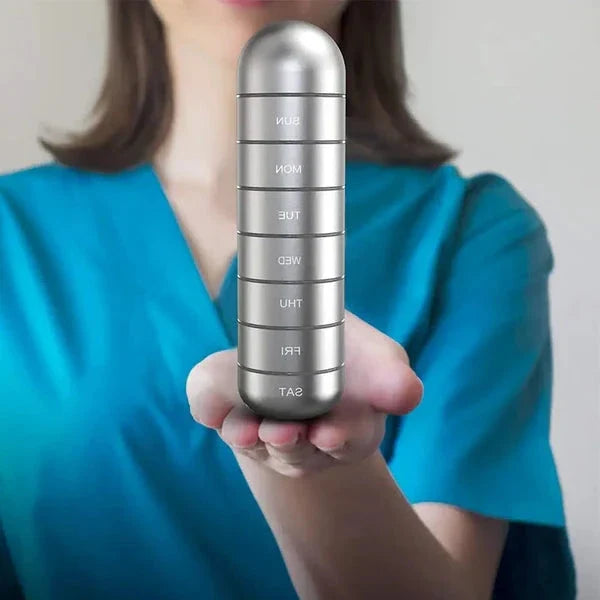 Silver aluminum weekly pill organizer held in hand, with labeled day compartments