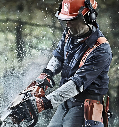 Chainsaw chain sharpener tool held by a worker wearing gloves and safety gear during use