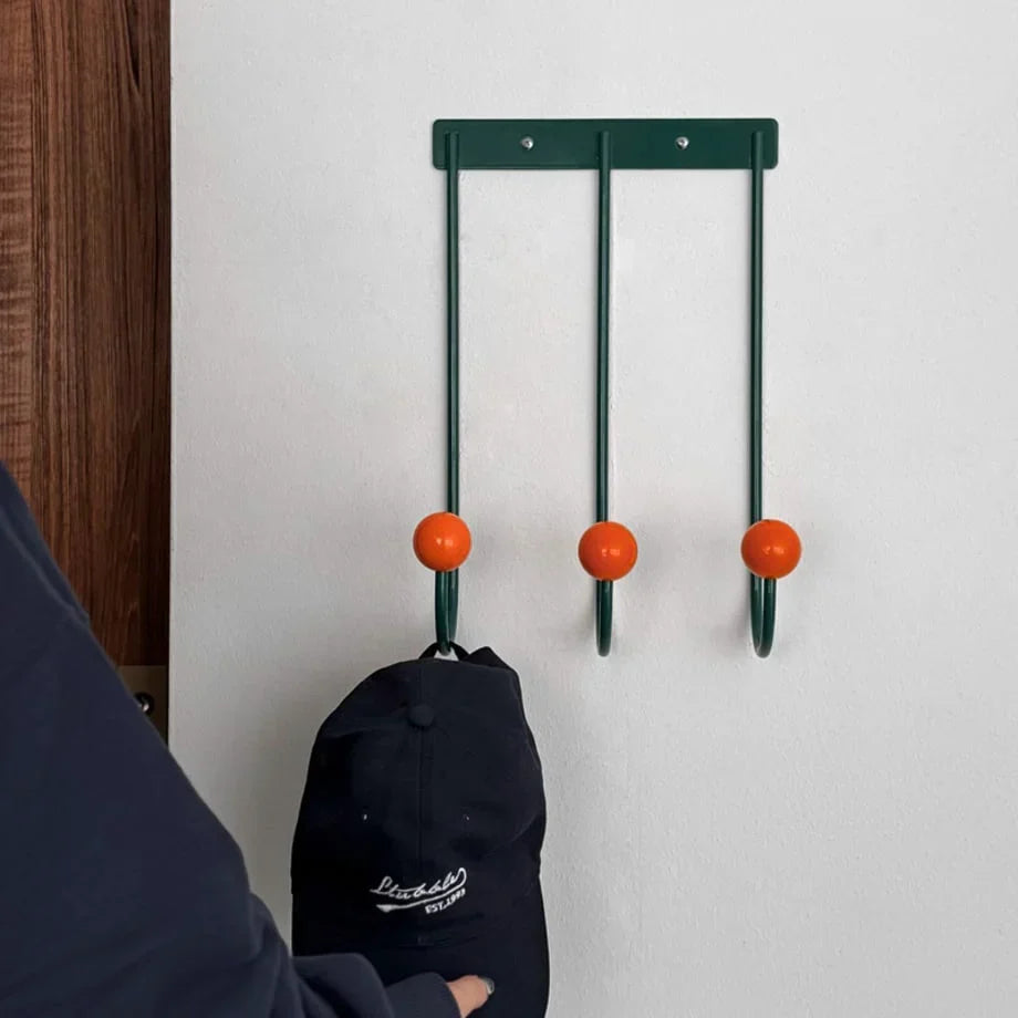 Metal wall hook rack with three curved hooks, orange ball knobs, and black bag hanging
