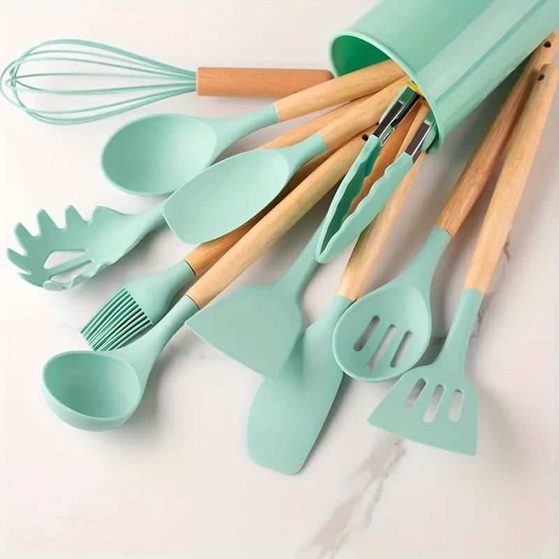 Light green silicone kitchen utensil set with light wood handles in matching holder