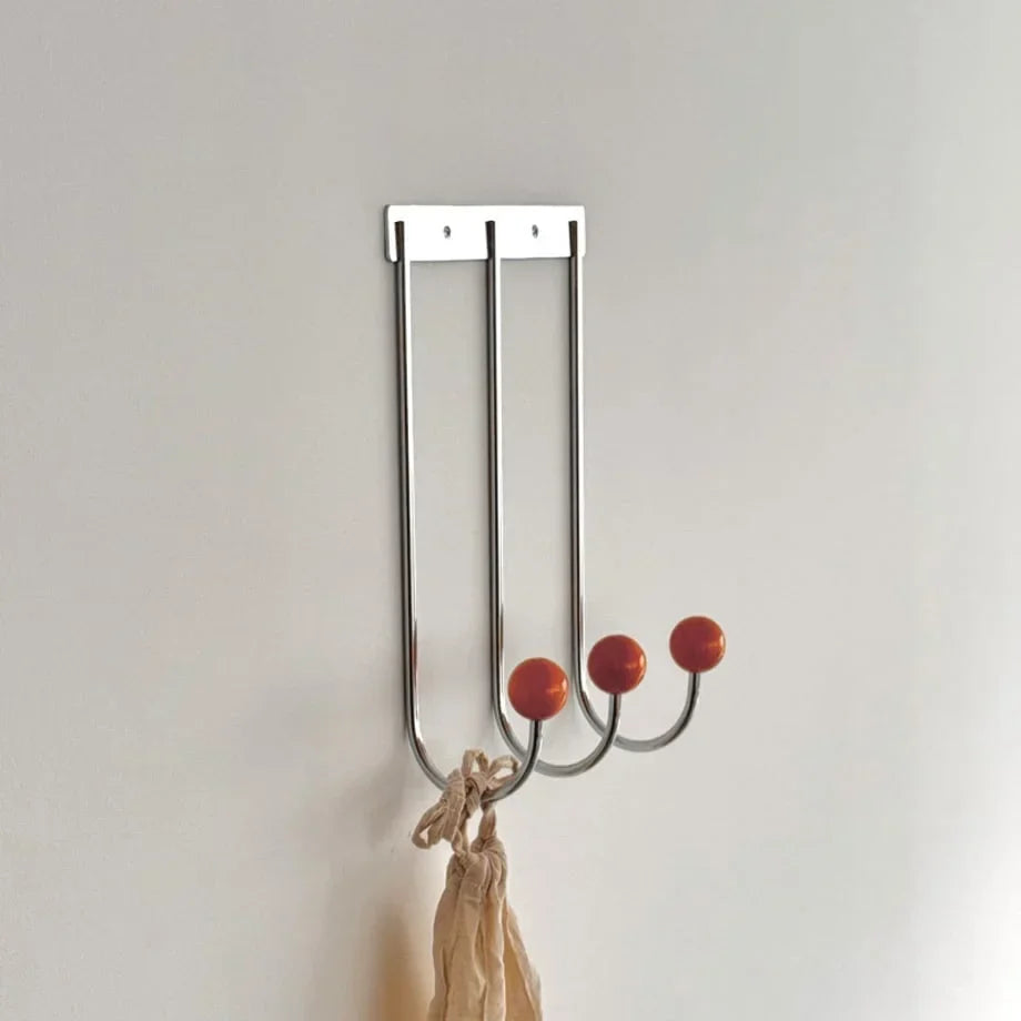 Metal wall hook rack with three curved hooks and orange-red ball knobs, beige bag hanging