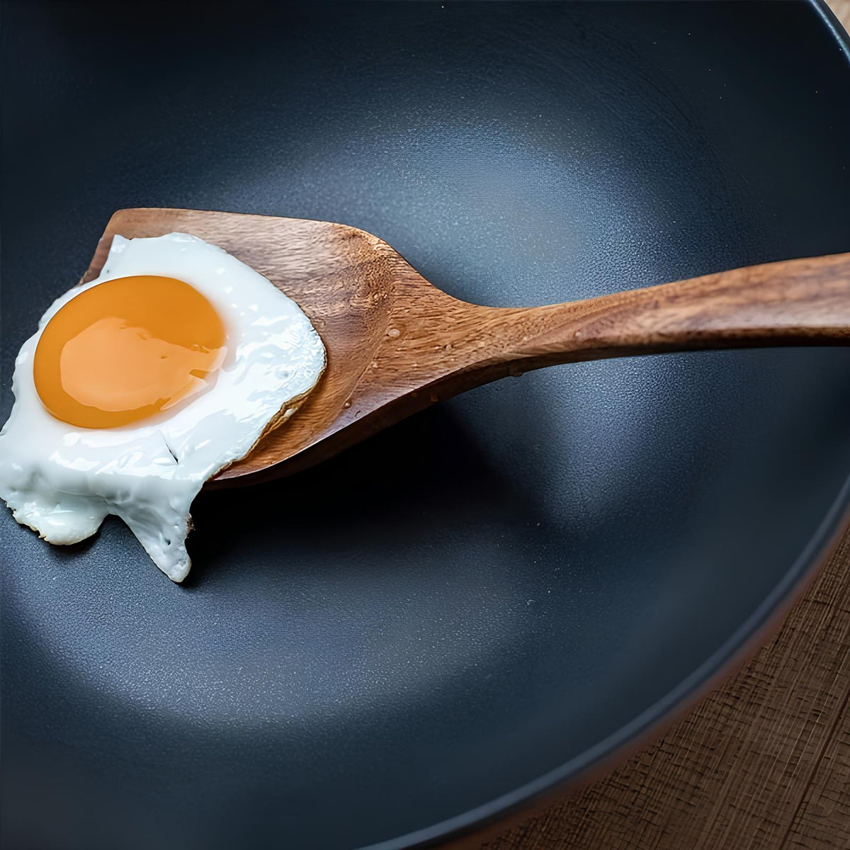 Teak wooden cooking spoon resting in a frying pan with a fried egg