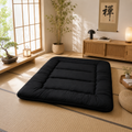 Black foldable floor futon mattress with quilted sections, laid flat on the floor