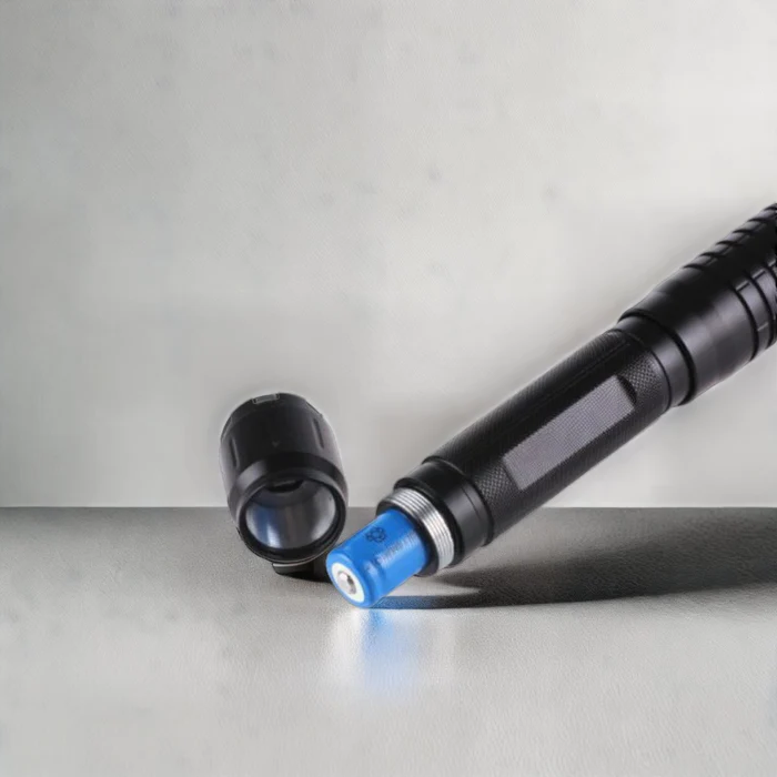 Black laser torch resting on surface, blue-white light at tip