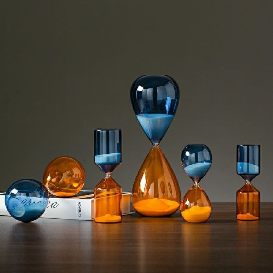 Set of colorful glass hourglasses on a dark surface with a neutral background