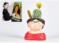 Ceramic face vase with red draped scarf, black hair, and cactus top