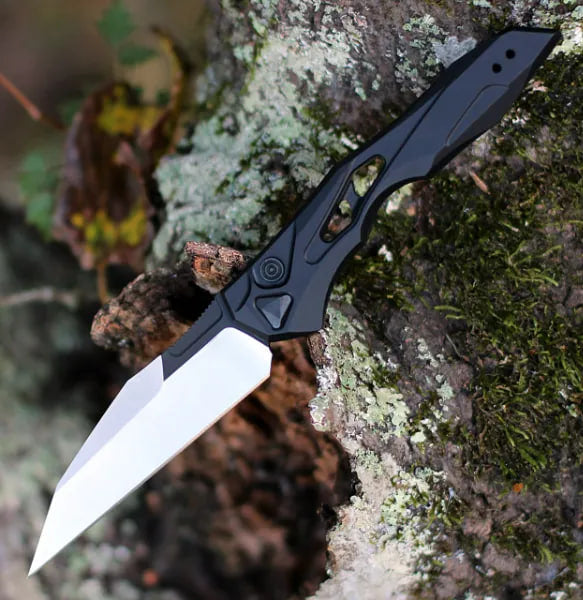 Black auto-fold utility knife with wharncliffe blade, angled view on rock