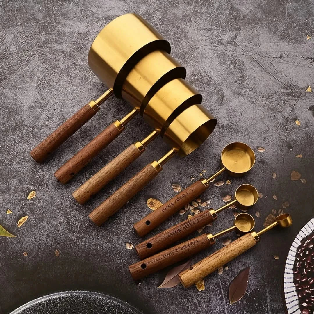 Gold measuring spoon set with wood handles, five stacked round metal measuring cups.