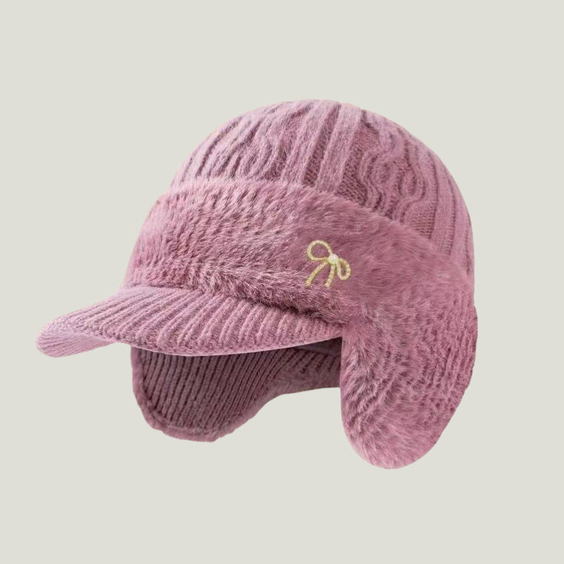 Pink fuzzy trapper ear flap hat with bow emblem and ribbed brim