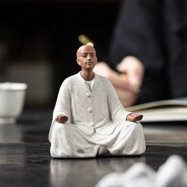 Seated monk statue with arms open and palms up, off-white speckled