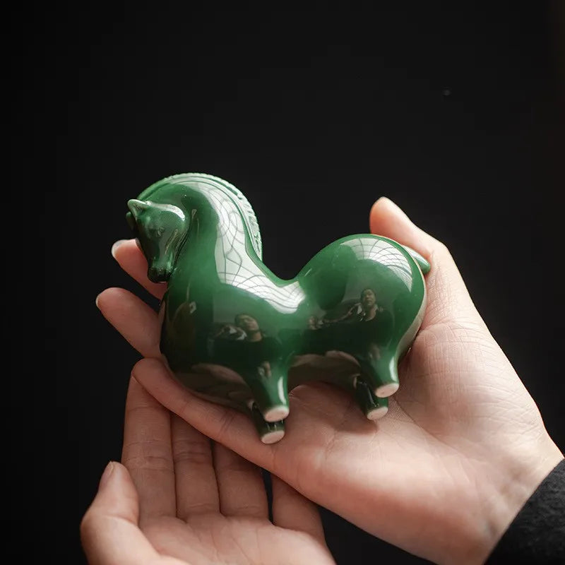 Ceramic horse figurine, dark green glossy glaze, held in a hand, side view.