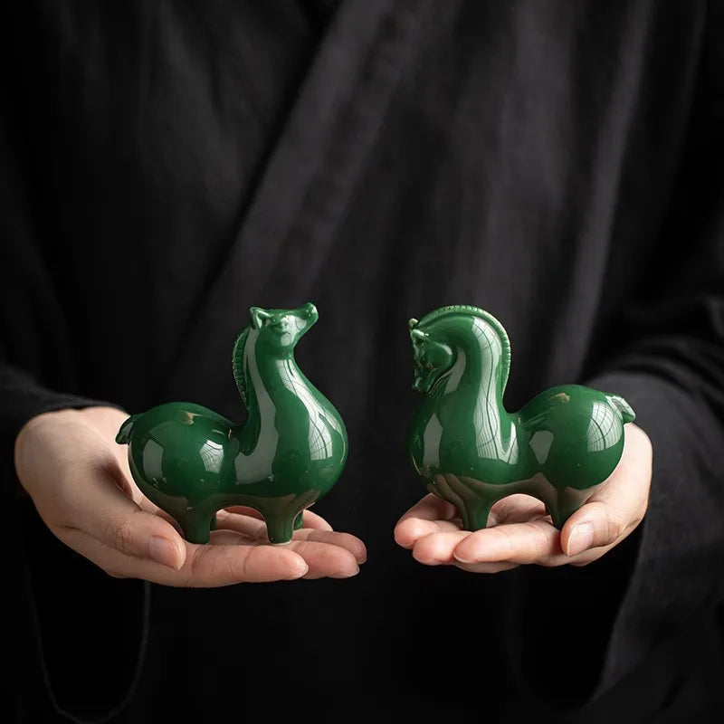 Ceramic horse figurines, dark green glossy glaze, held in two hands.