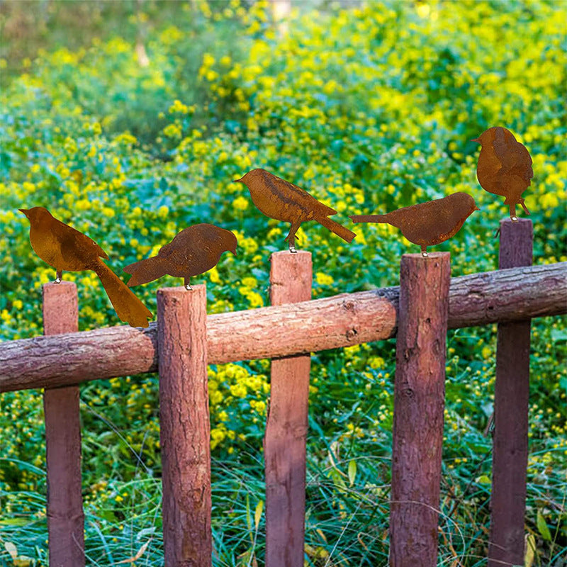 Metal bird sculptures on a wooden fence with a blurred natural background