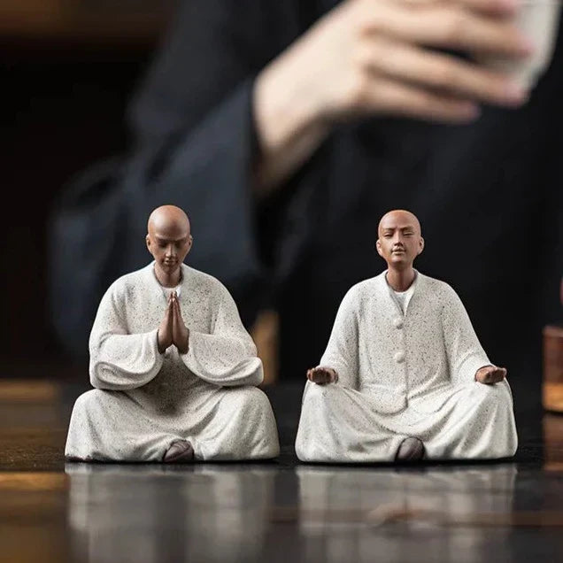 Pair of seated monk statues, palms together and open hands, off-white speckled