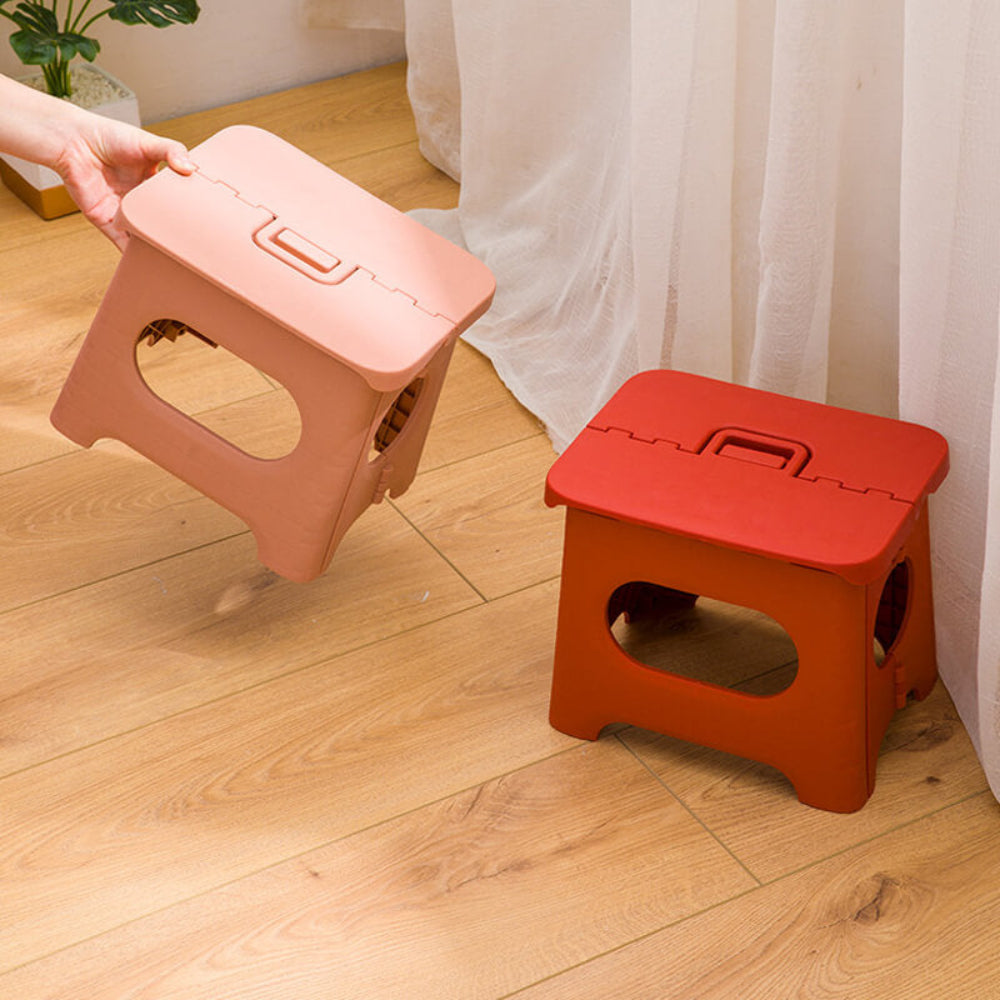 Foldable step stool in pink and orange with oval safety cutouts and hinged top.