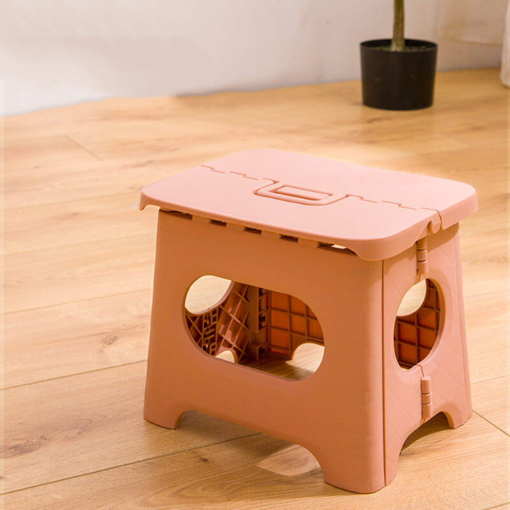 Foldable step stool in light pink with oval safety cutout and top carrying handle.