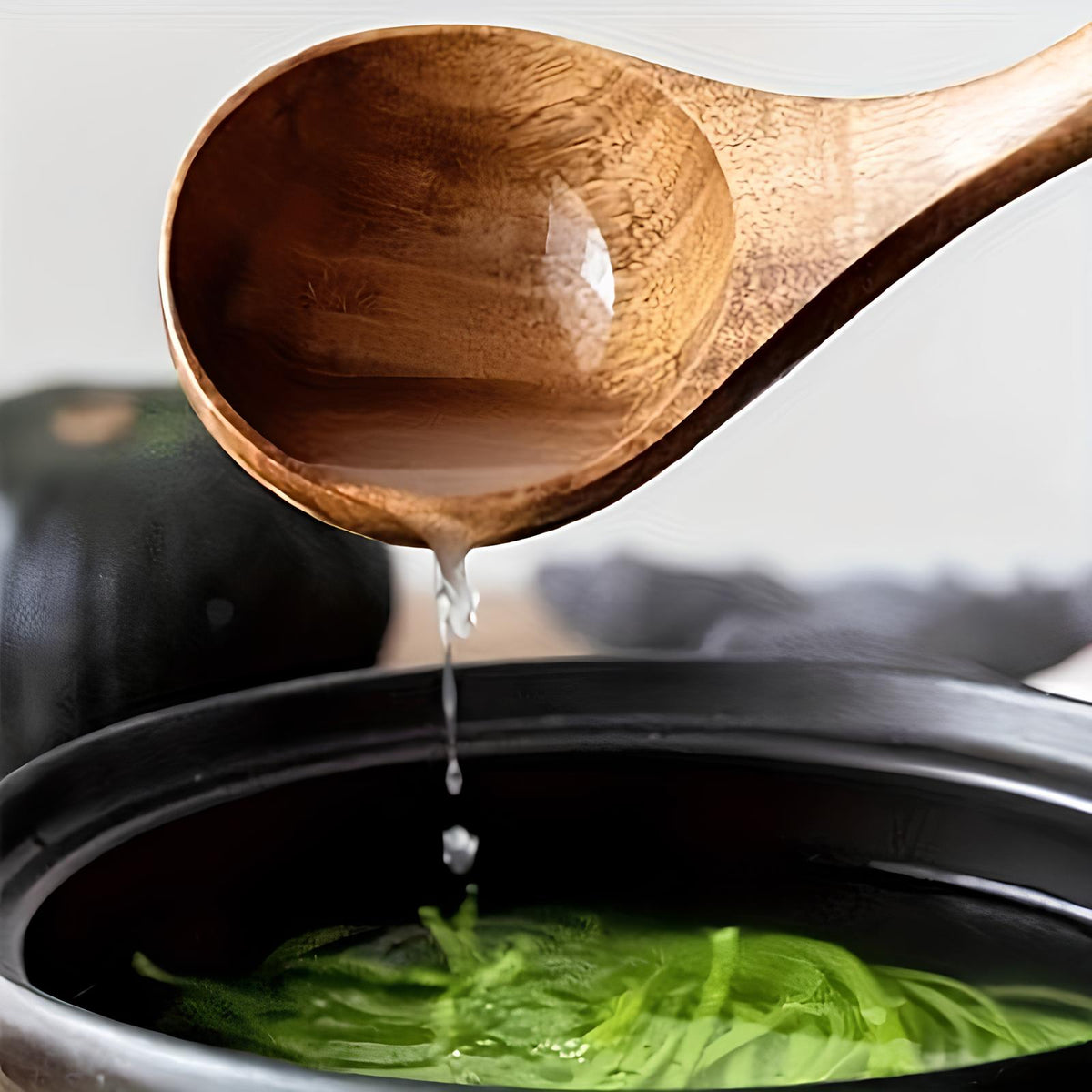 Teak wooden ladle pouring greens from a pot