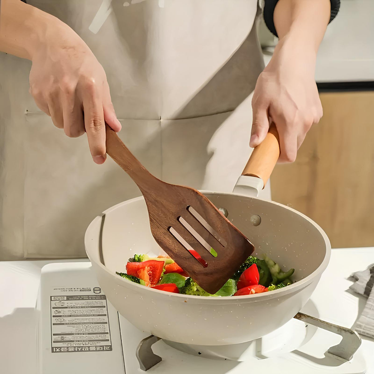Teak kitchen utensil spatula stirring vegetables in a white pot