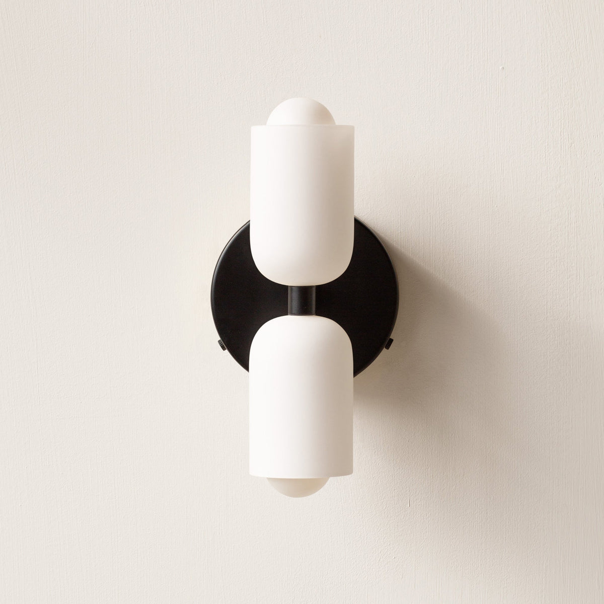 Black wall sconce lamp with two frosted cylindrical acrylic shades and round metal disc