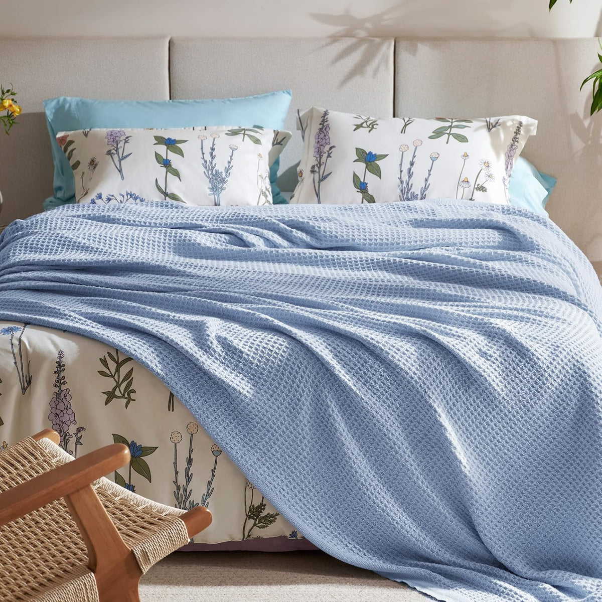 Light blue cotton waffle-weave cooling blanket draped across a bed with floral pillows.
