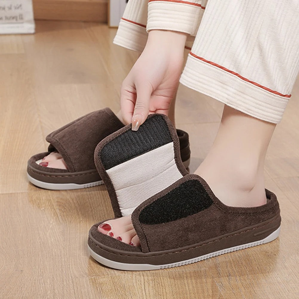 Brown slippers with a striped sole held by a person on a wooden floor.