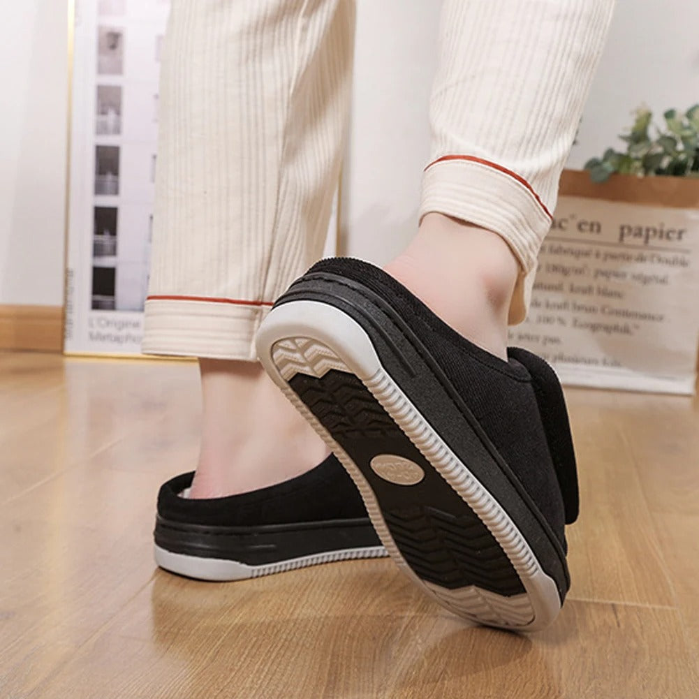 Person wearing black slip-on shoes with white soles on a wooden floor.