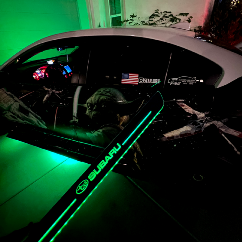 Car interior with green lighting and visible Subaru logo, American flag, and text on dashboard.