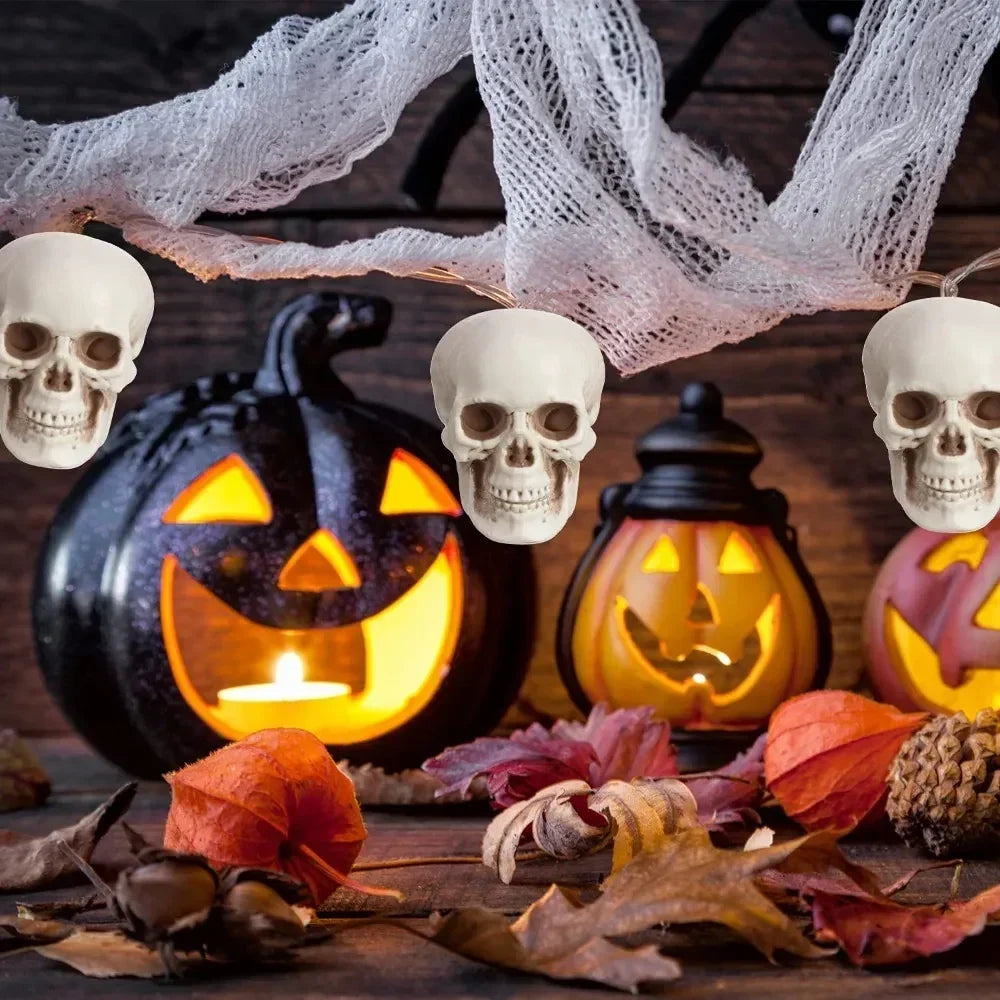Mini white skeleton skull ornaments hanging in white web, with carved pumpkin lights