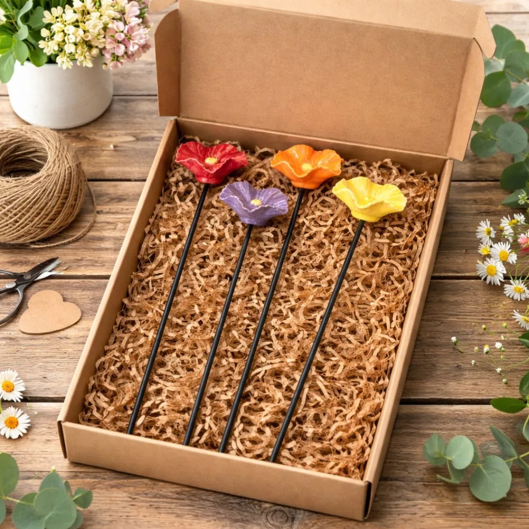 Colorful flower-shaped candles in a cardboard box on a wooden surface with floral decorations.