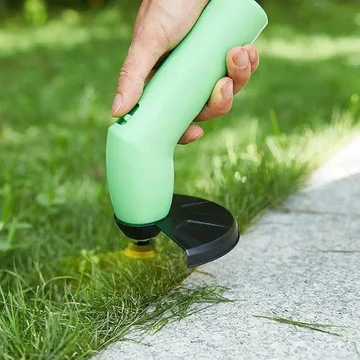 Cordless mini weed trimmer cutting along pavement edge, green nozzle and black guard