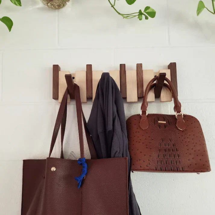 Wooden fold-out wall hook rack with open pegs holding handbags and coats