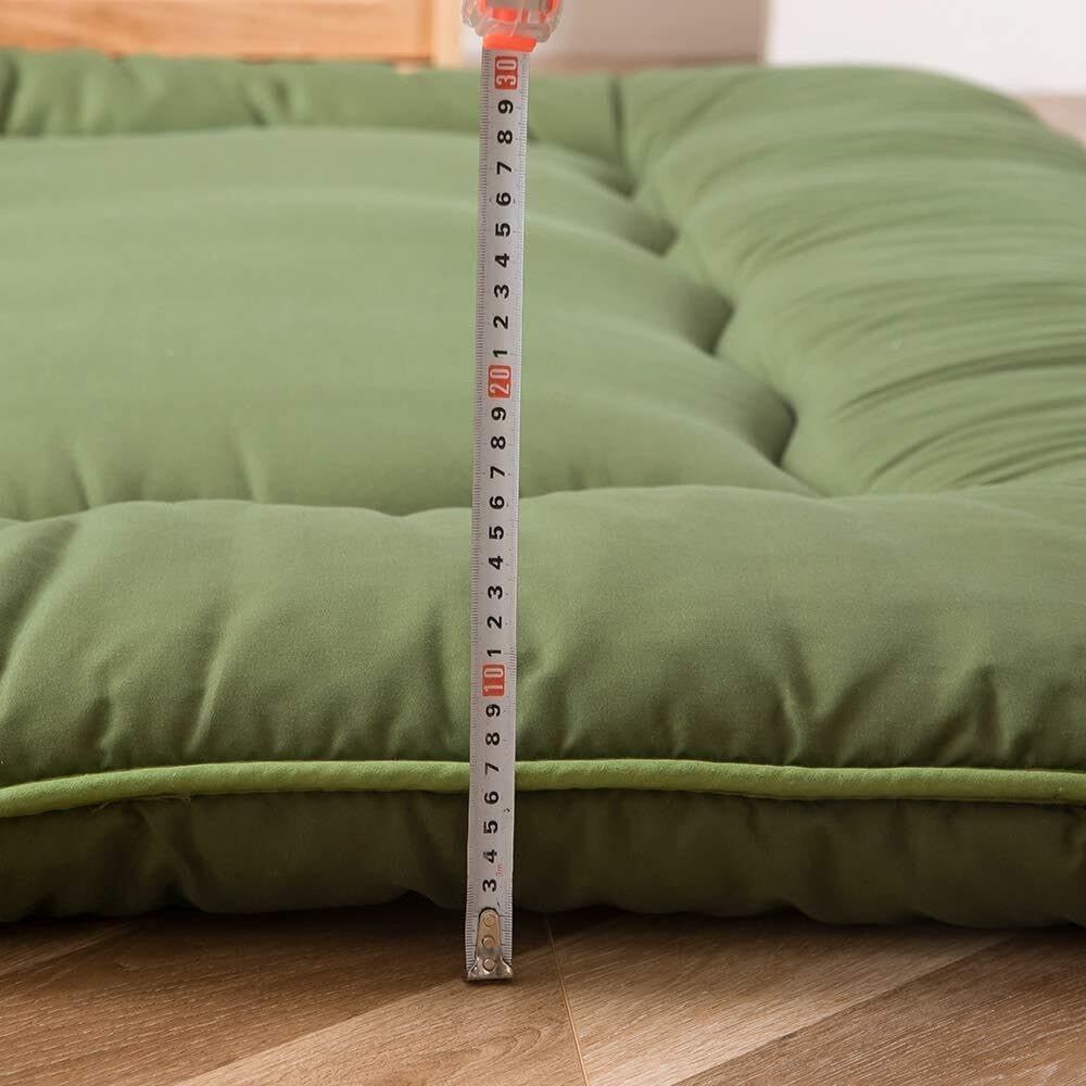Green foldable floor futon mattress with measuring tape showing thickness