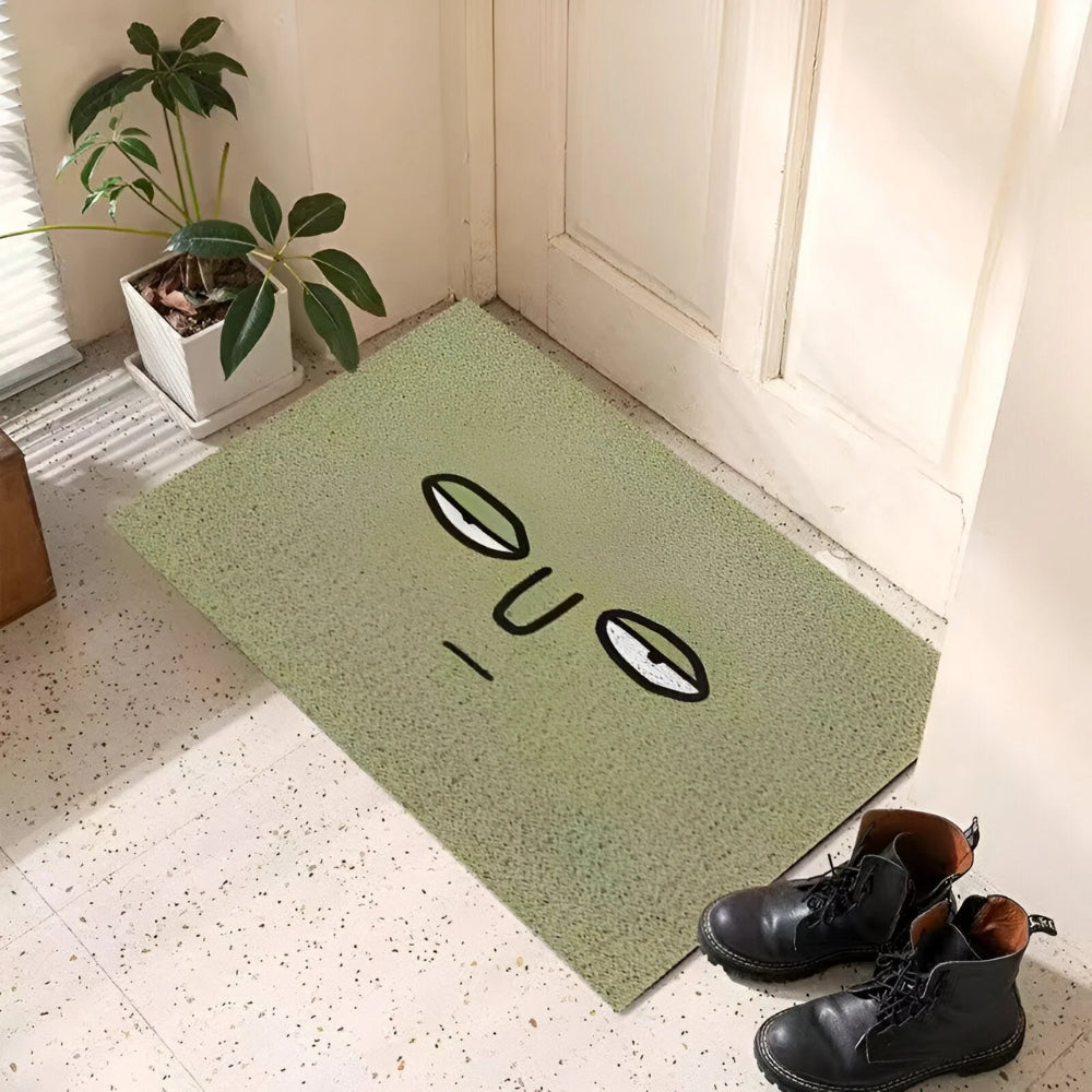Green speckled entrance doormat with black oval eyes and curved smile