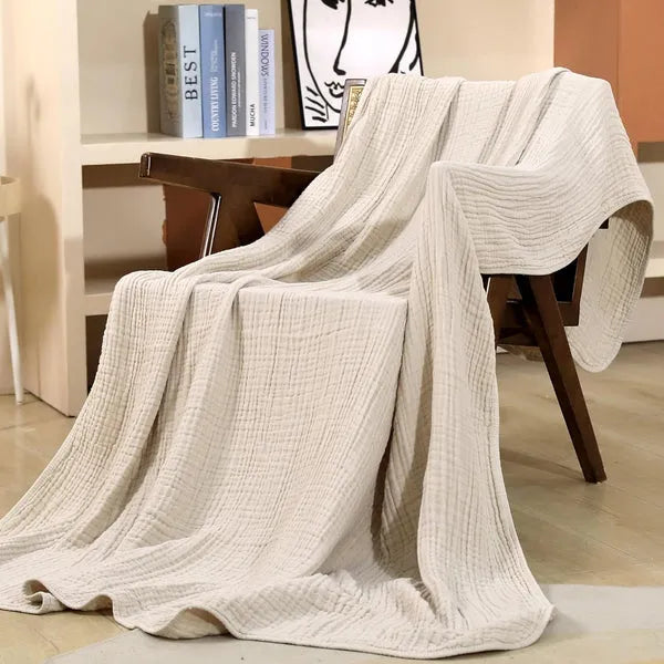 White cotton muslin throw blanket draped over a chair, crinkle weave texture visible