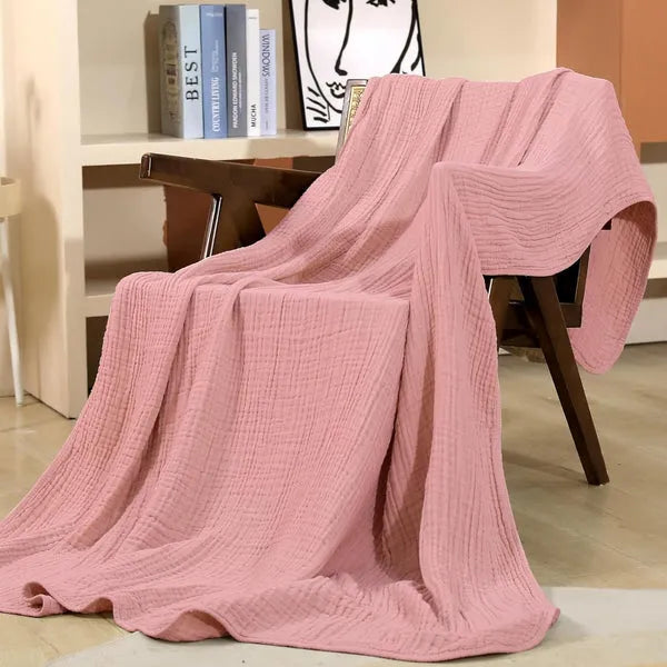 Pink cotton muslin throw blanket draped over a chair, soft crinkle texture