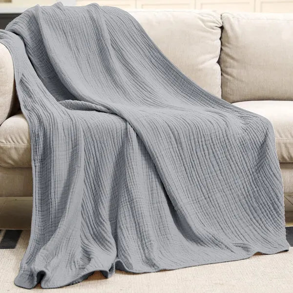 Gray cotton muslin throw blanket draped over a sofa, showing crinkle weave texture