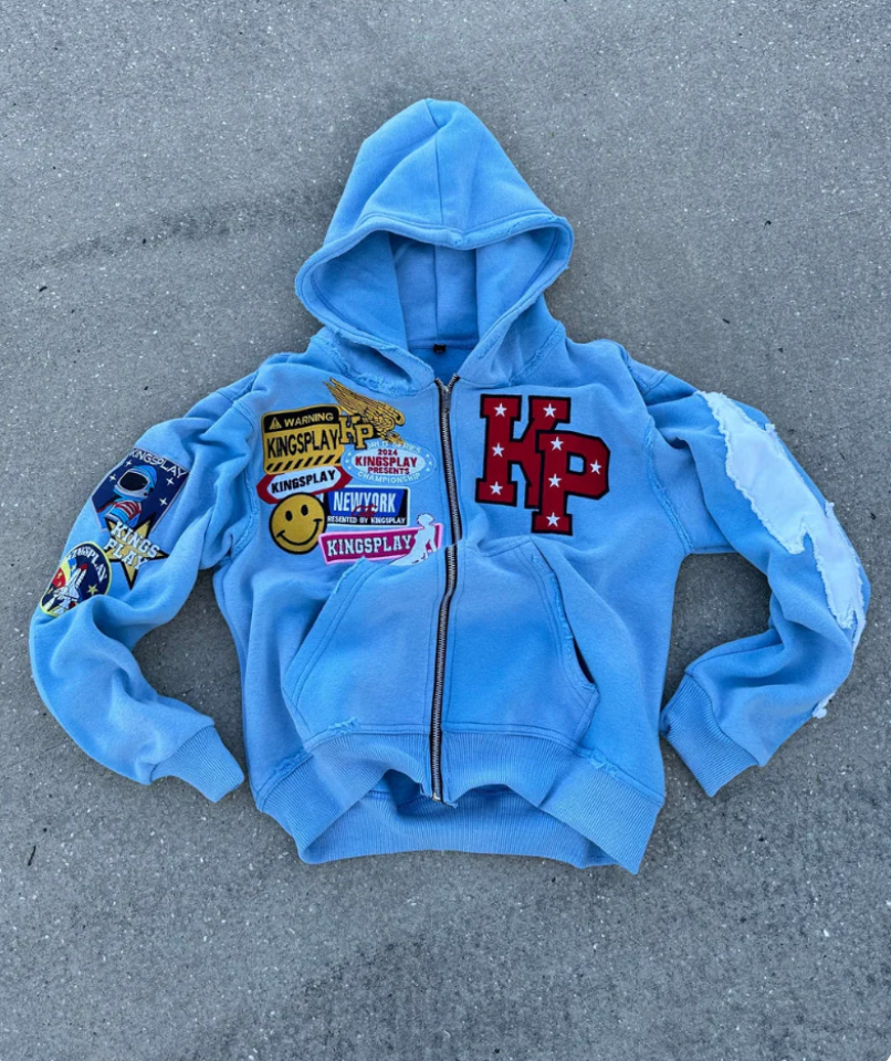 Blue zip-up hoodie jacket with hood, front pocket, and colorful graphic patches