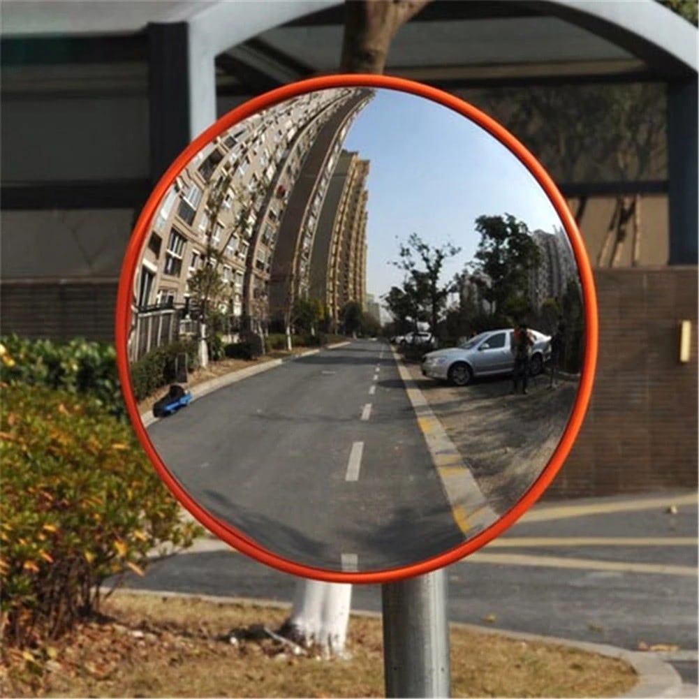 Circular wide-angle mirror with orange border mounted on a pole, street reflection