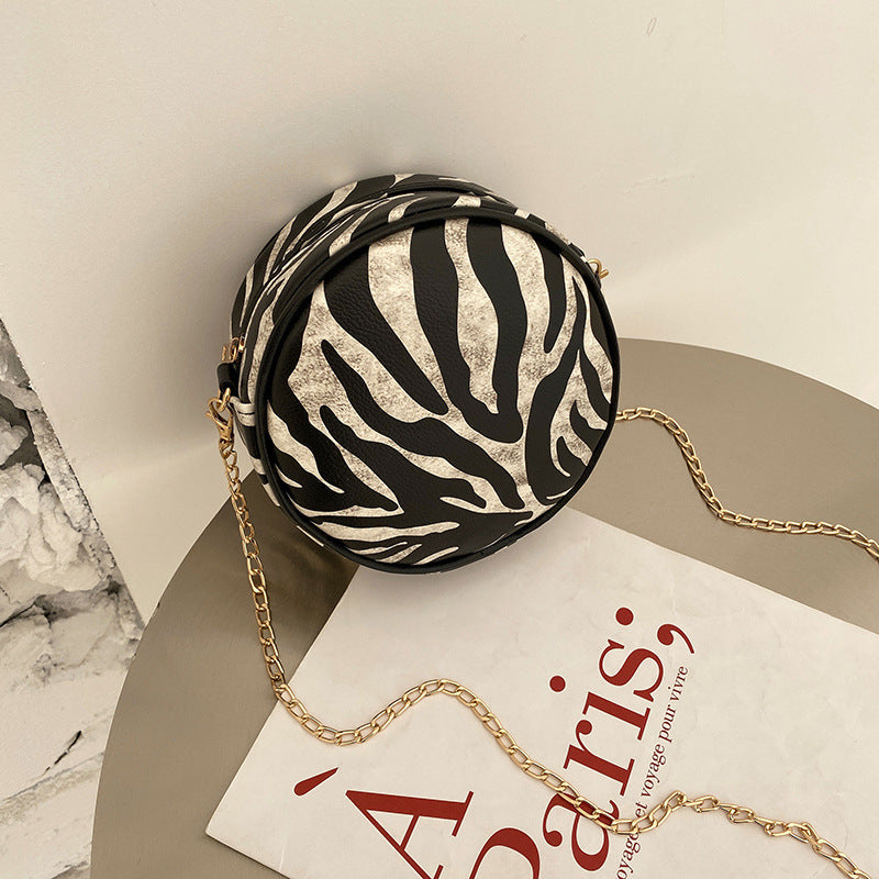 Zebra-pattern round mini crossbody bag with gold-tone chain strap and zipper top