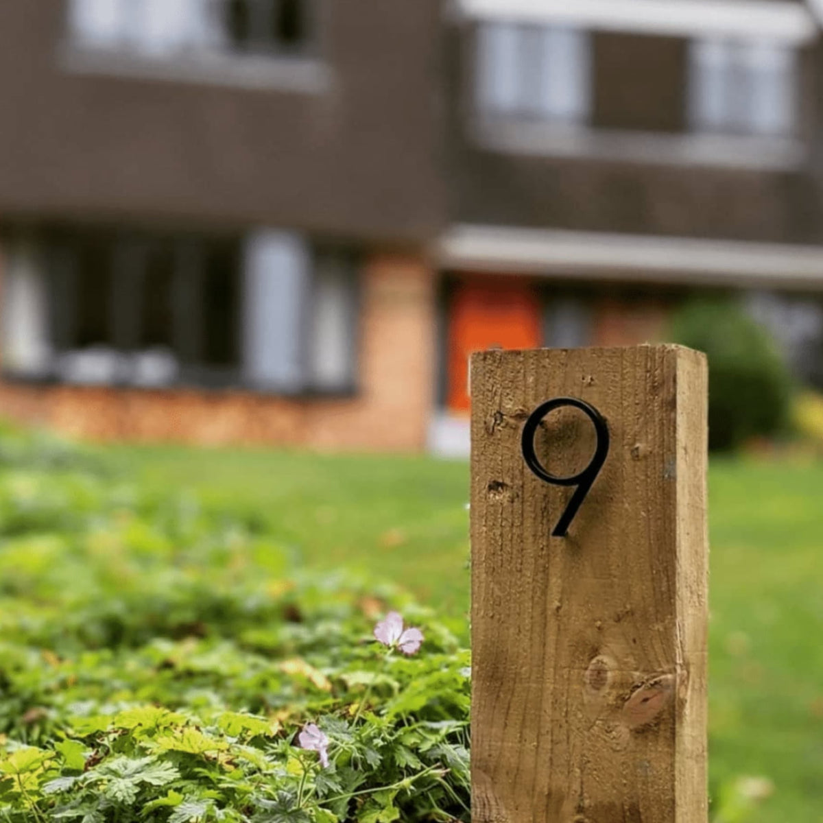 Dark metal house number 9 on a wooden post