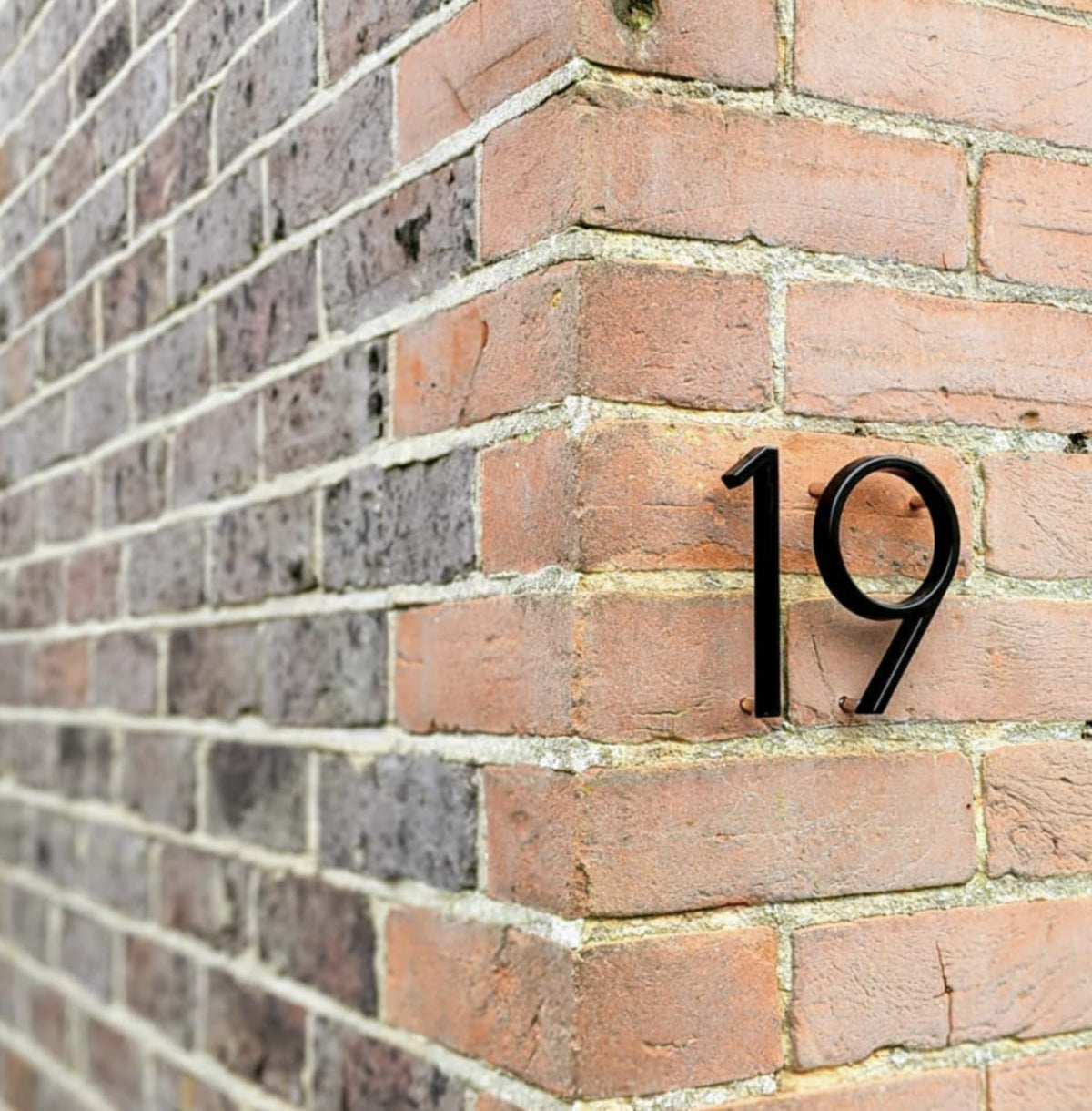 Black metal house number 19 on a brick wall, raised numerals